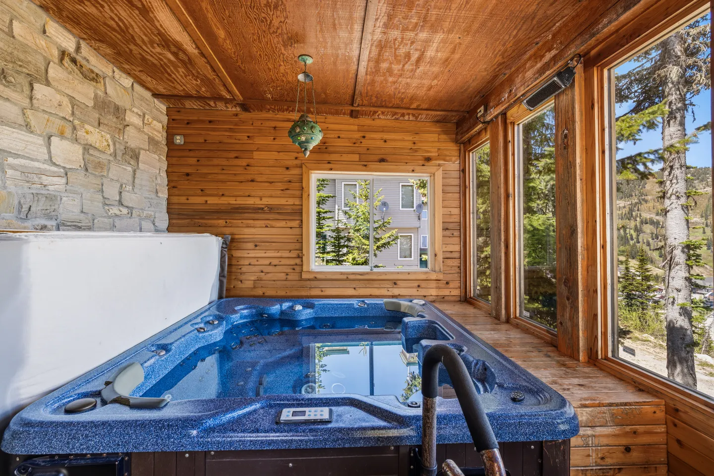 Indoor hot tub room with wood-paneled walls and ceiling, large windows, and a stone accent wall.