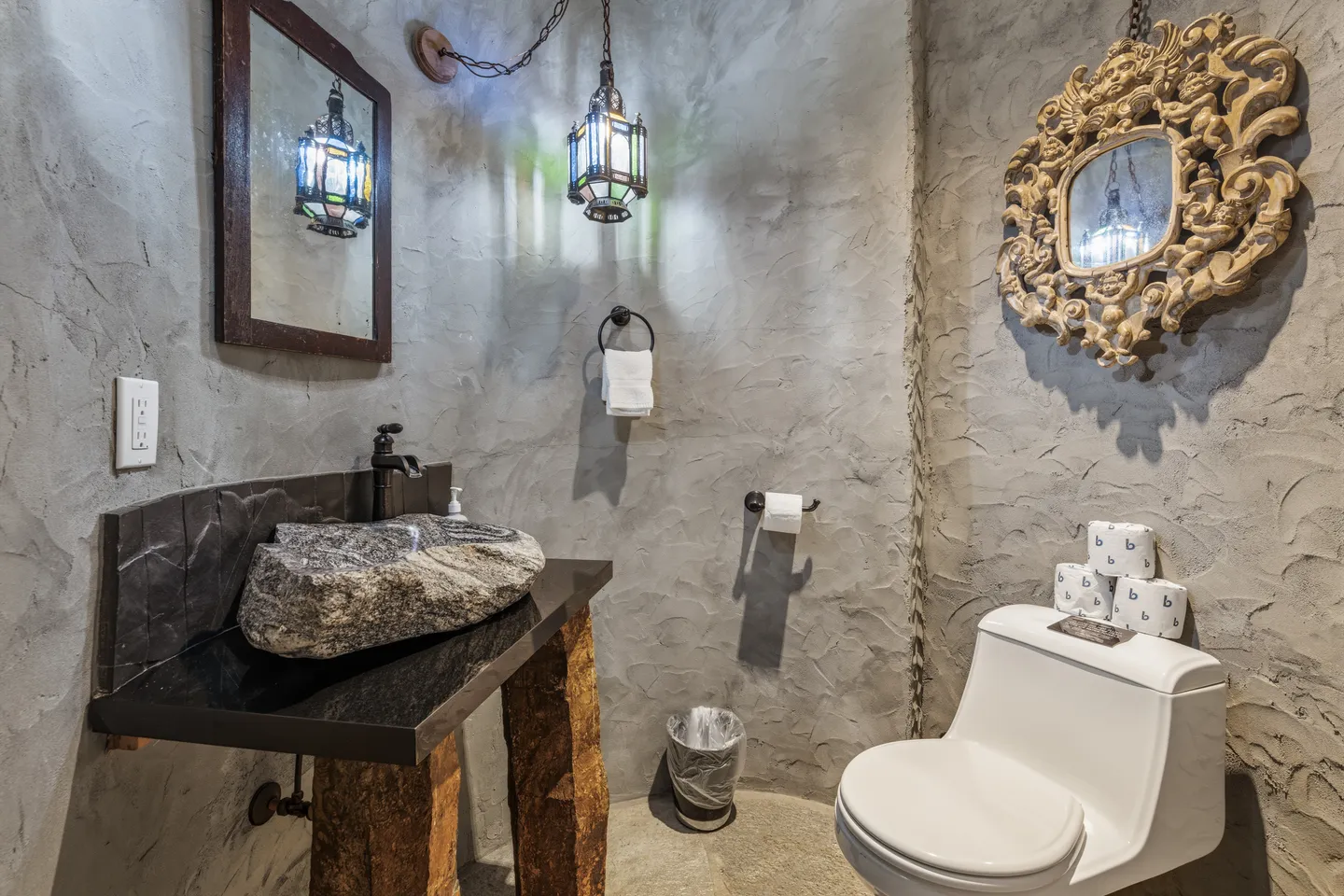 Bathroom with textured gray plaster walls, a stone vessel sink on a rustic vanity, and a white toilet.