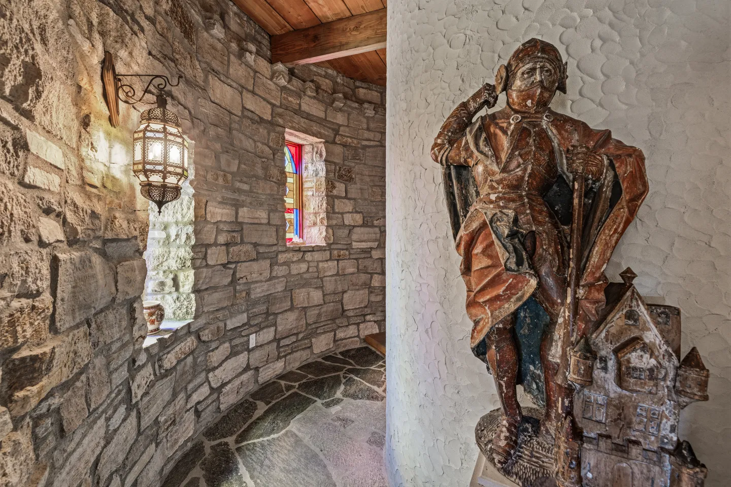 Curved stone hallway with a knight statue, a hanging decorative lantern, and a stained glass window.