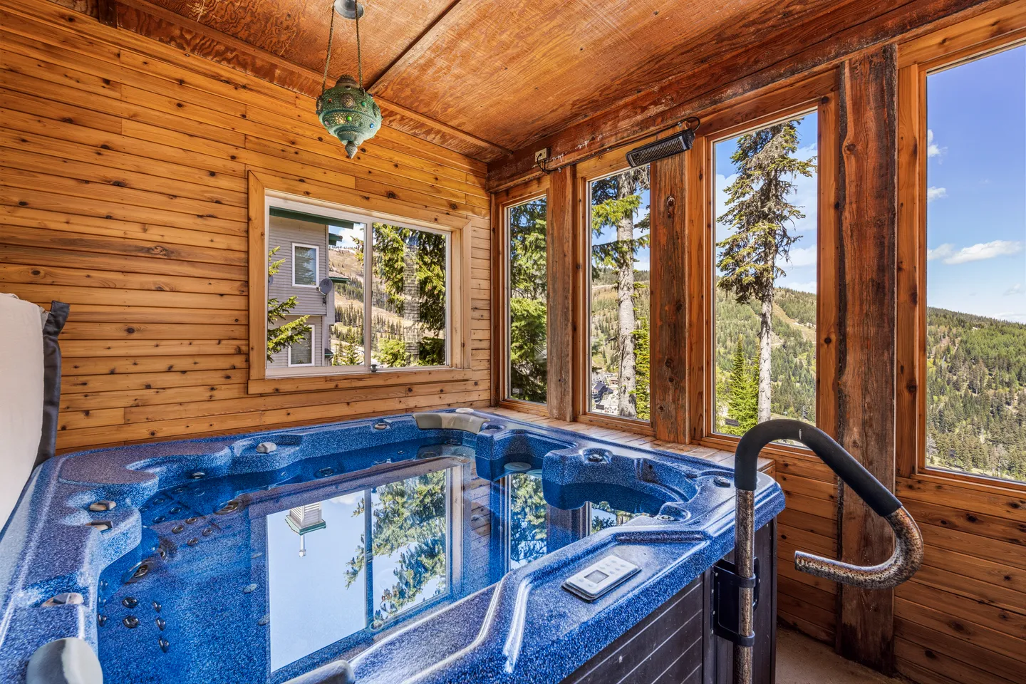 Indoor hot tub filled with clear water set inside a wood-paneled room with large windows overlooking forested hills.