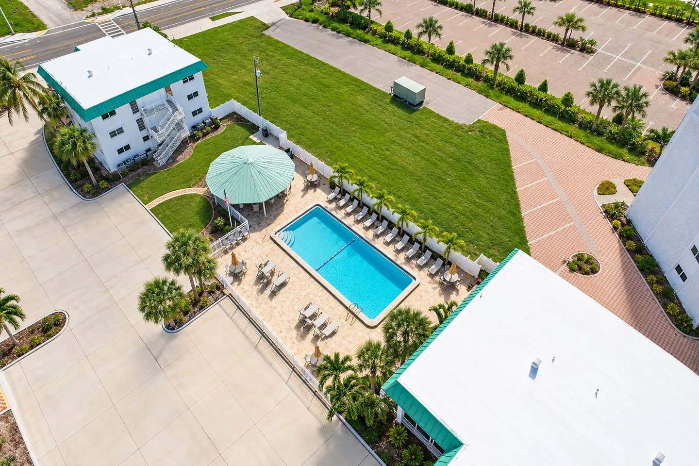 Aerial view of an outdoor community swimming pool surrounded by a patio, lounge chairs, a gazebo, and grassy lawn.