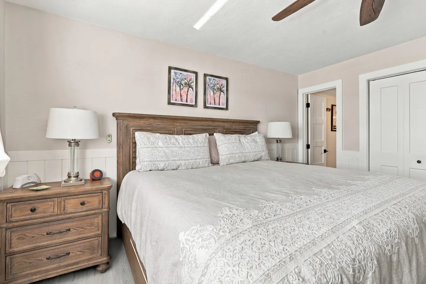 Bedroom featuring a large bed with a wooden headboard, light gray patterned bedding, a matching wooden nightstand, and framed artwork.