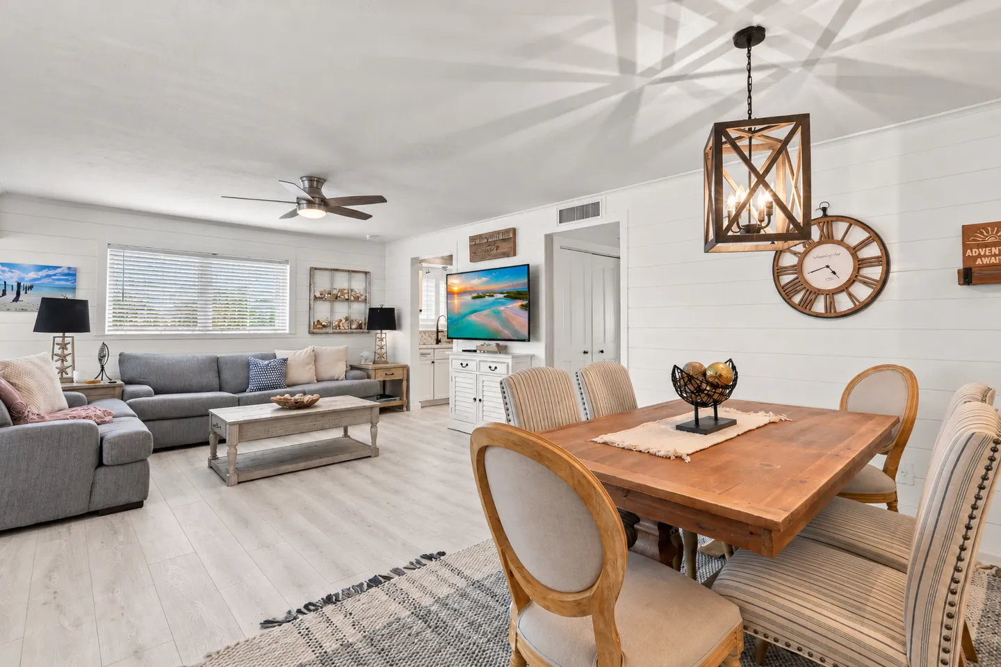 Open-concept living and dining area with light wood-style flooring, a wooden dining table, a grey sectional sofa, and a wall-mounted TV.