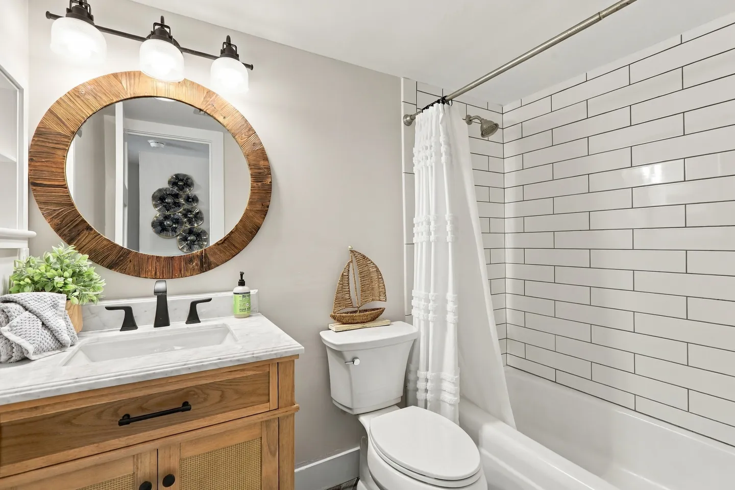 Bathroom with a wood vanity, round wooden mirror, white toilet, and subway-tiled shower and tub combination.