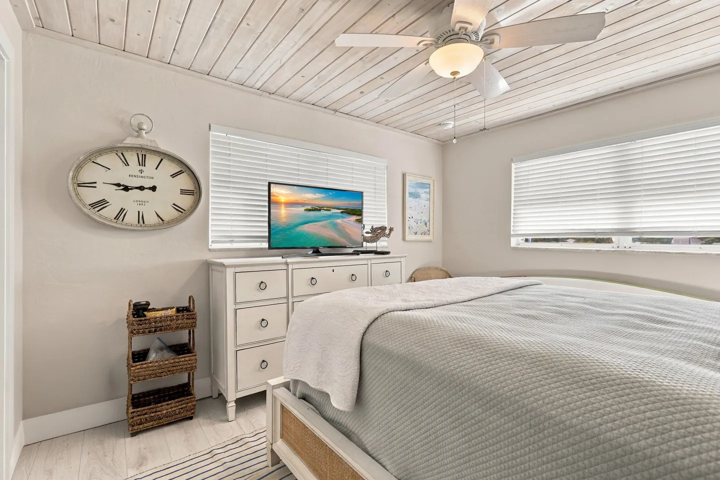 Bedroom featuring a bed with a textured grey quilt, a white dresser with a television, and a wood plank ceiling with a ceiling fan.