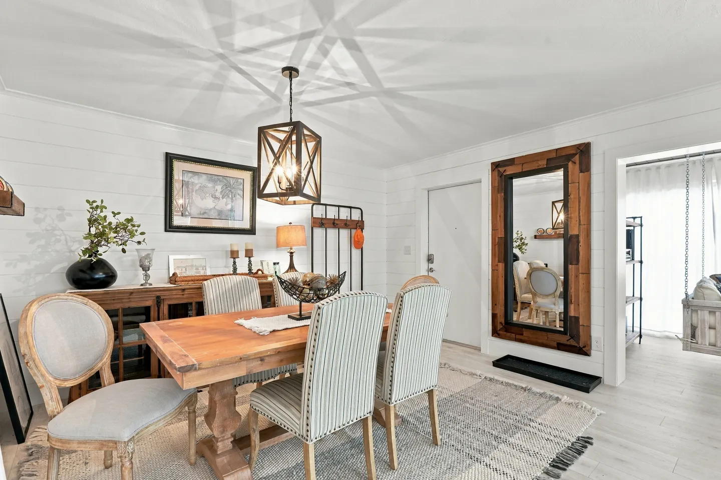 Dining area with a wooden table, striped and upholstered chairs, a hanging geometric light fixture, and white shiplap walls.
