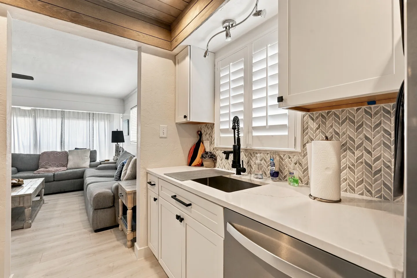 Kitchen counter and sink with view into an adjacent living room with a sectional couch.