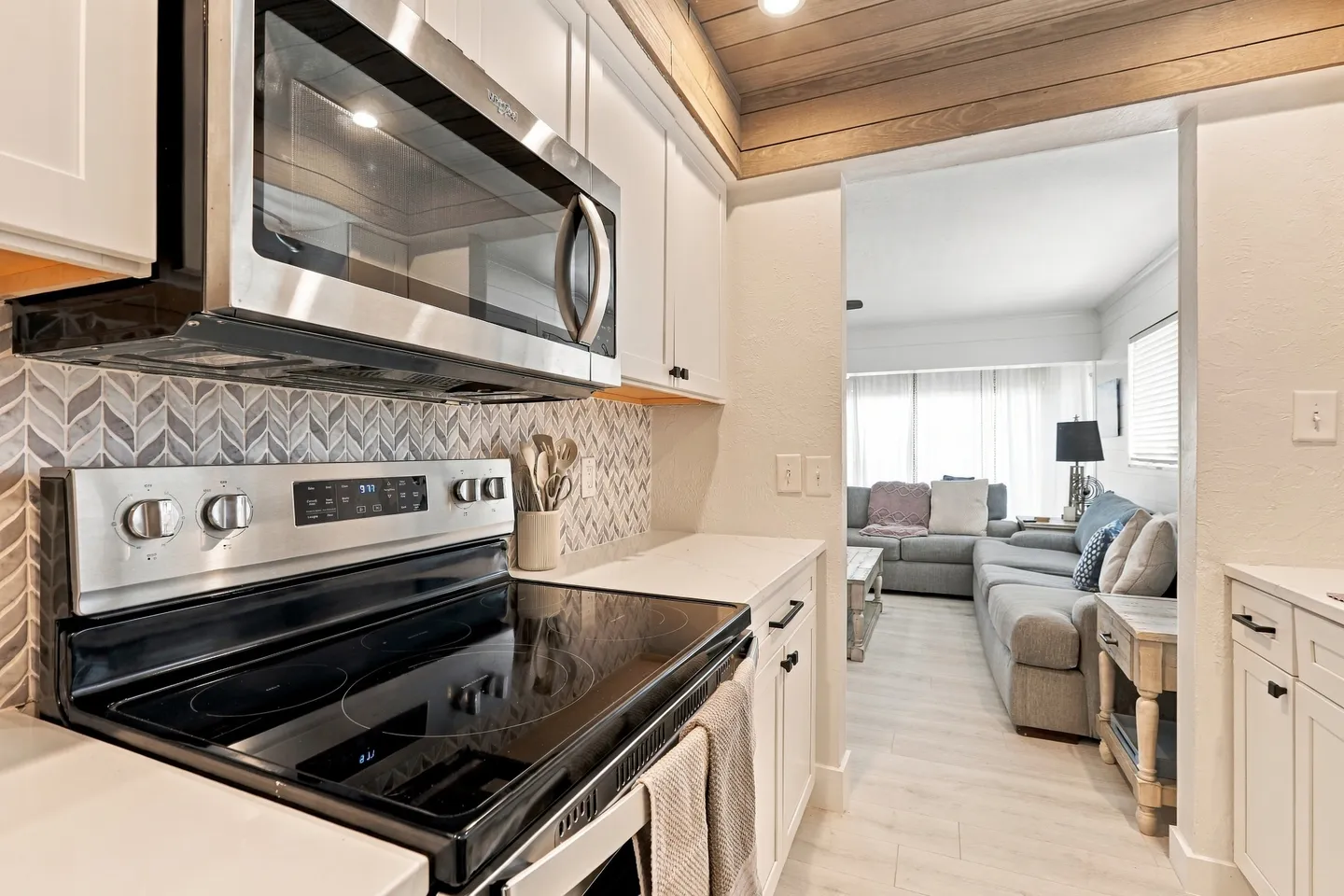 Close-up view of a modern kitchen with stainless steel appliances looking through a doorway into the adjacent living room.