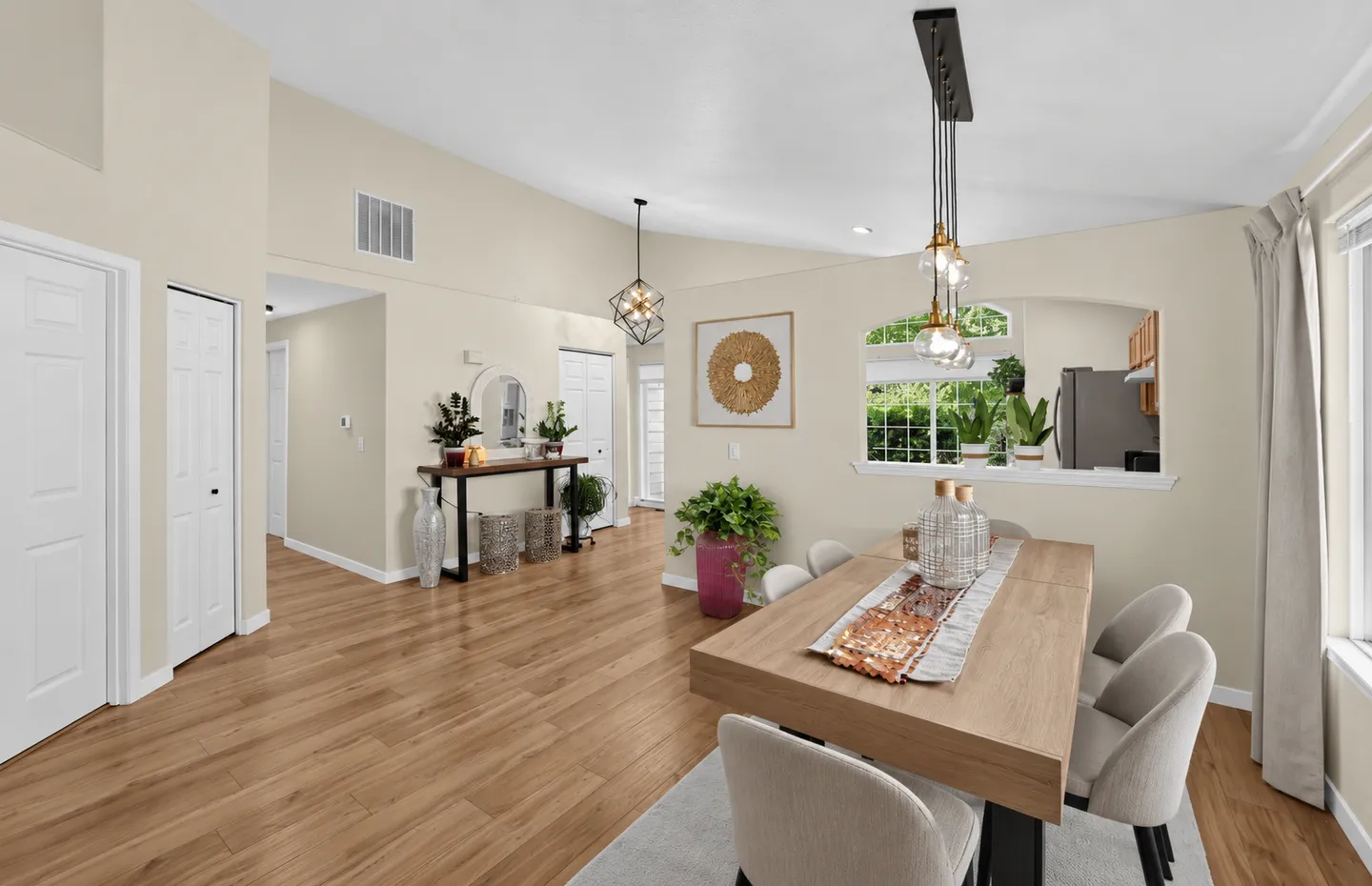 Dining area with a wood table, modern pendant lighting, wood-style flooring, and a pass-through cutout to the kitchen.