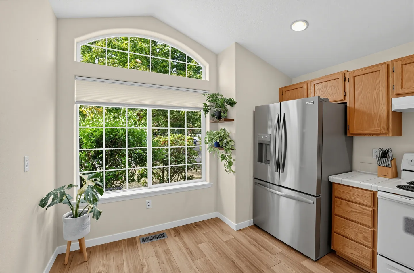 Kitchen nook with a large arched window, wood-look flooring, stainless steel refrigerator, and wood cabinets.