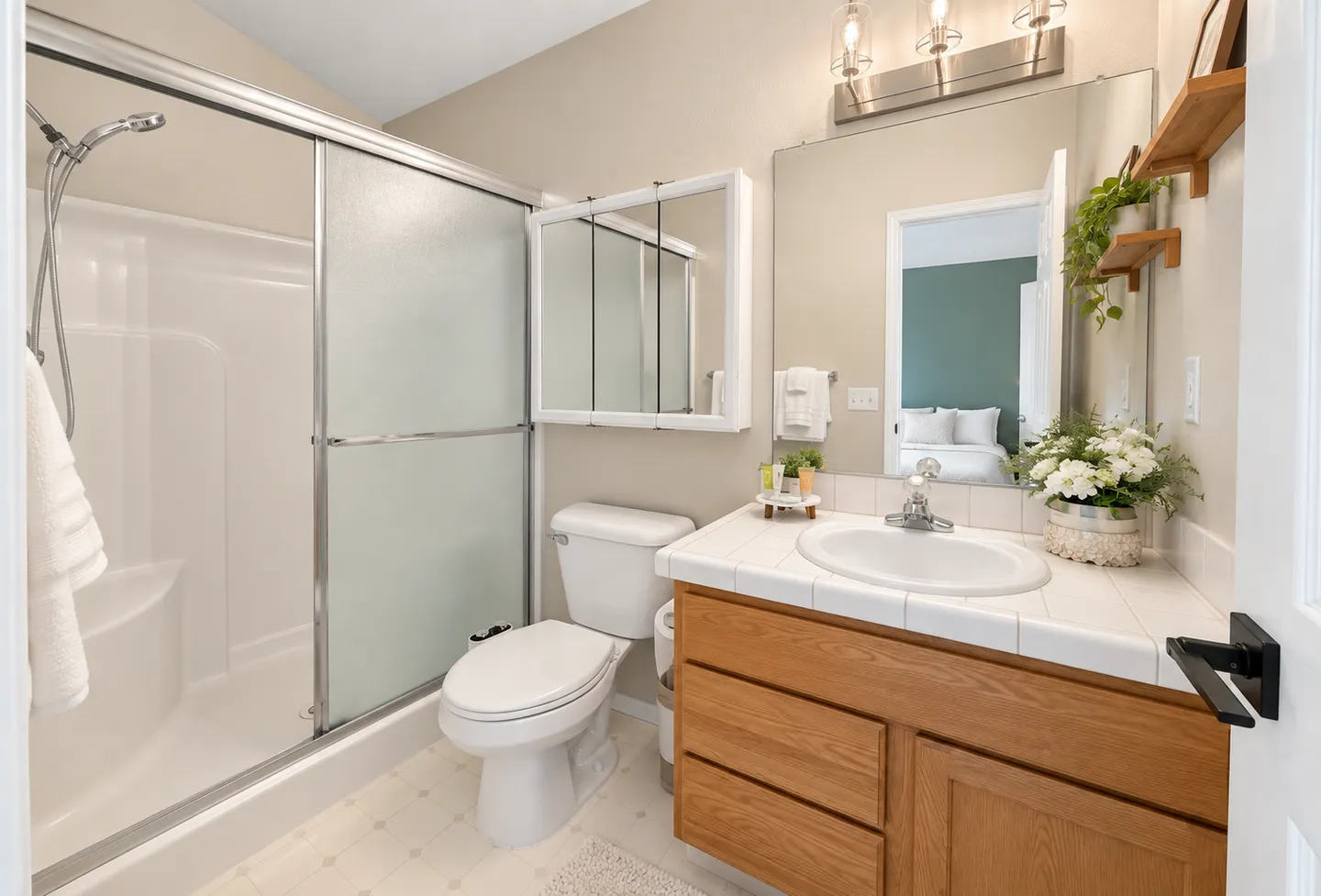 Bathroom with a glass-enclosed bathtub shower combo, toilet, and wood vanity with white tile countertop.