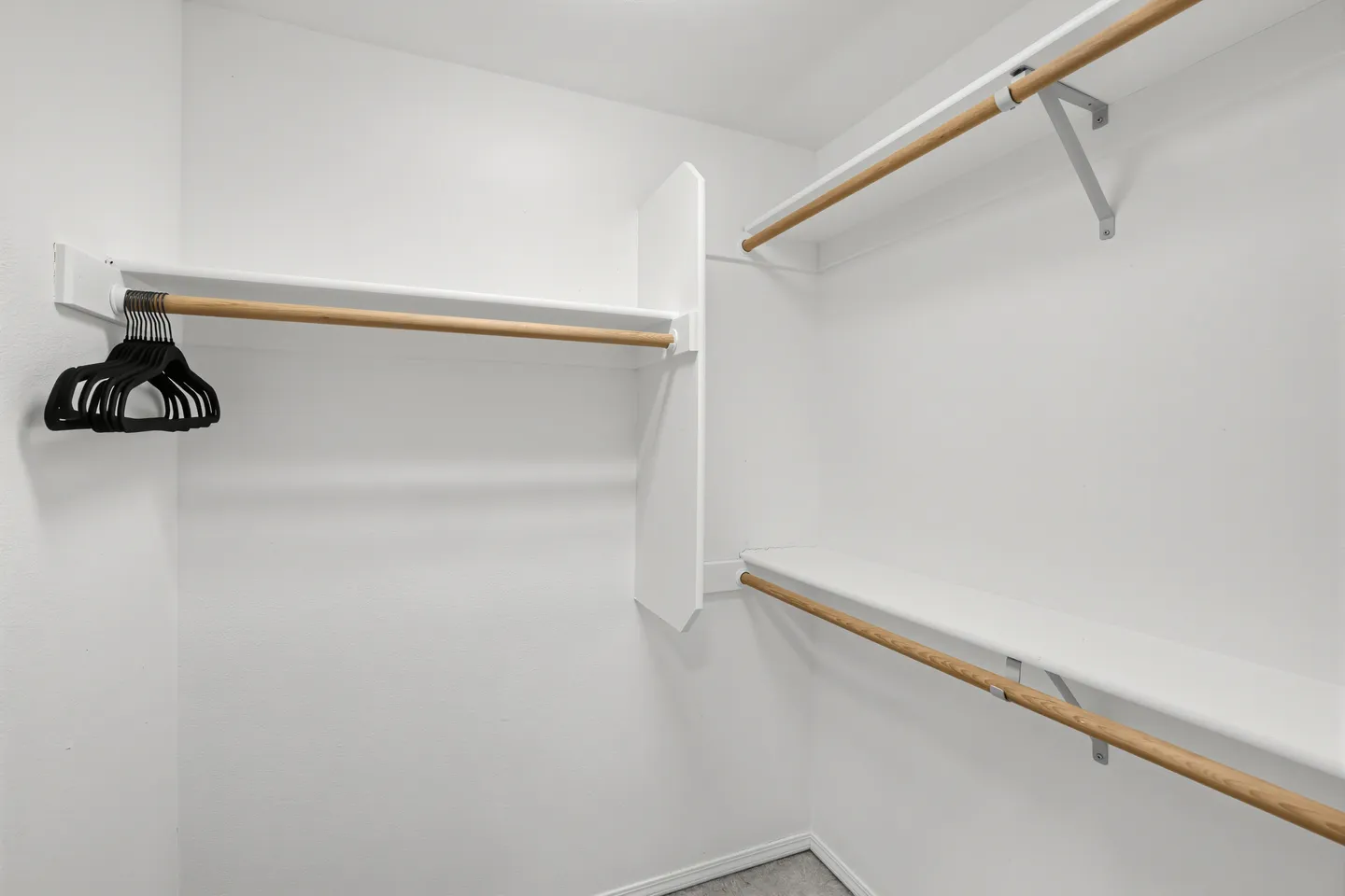 A walk-in closet with white walls, shelves, wooden hanging rods, and several black clothes hangers.