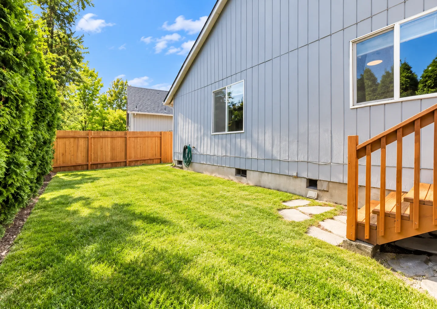 Grassy side yard of a home with light blue siding, a wooden fence, and wooden exterior steps.