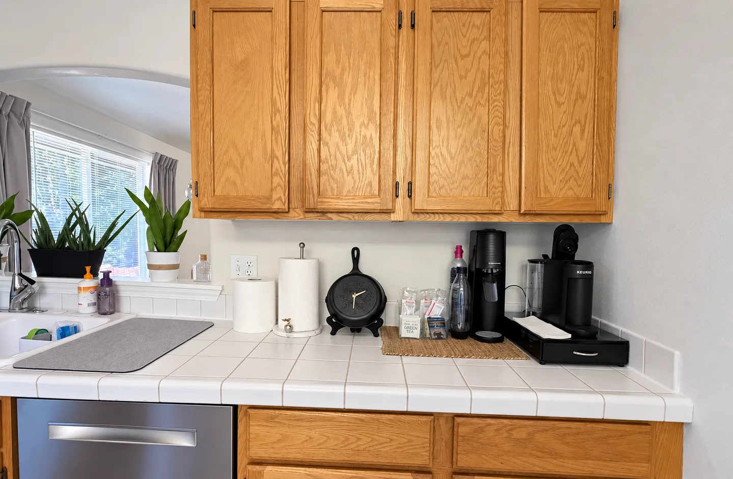 Kitchen counter with white tile, wood cabinets, a dishwasher, a sink, and a coffee and beverage station.