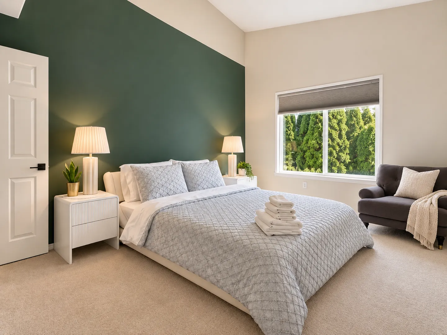 Bedroom with a green accent wall, made bed with folded towels, nightstands with lamps, carpeted floor, and a window.