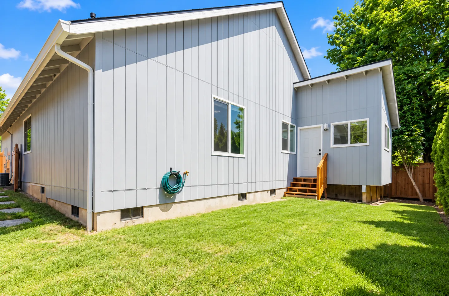 Exterior backyard view of a light blue house with vertical siding and a grassy lawn.