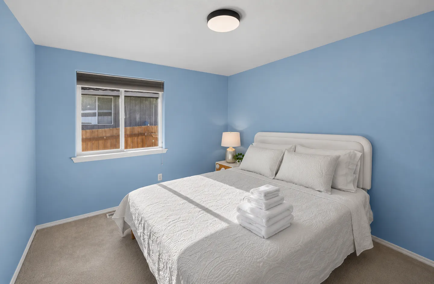 Bedroom with light blue walls, carpeted floor, a bed with white bedding, and a window.