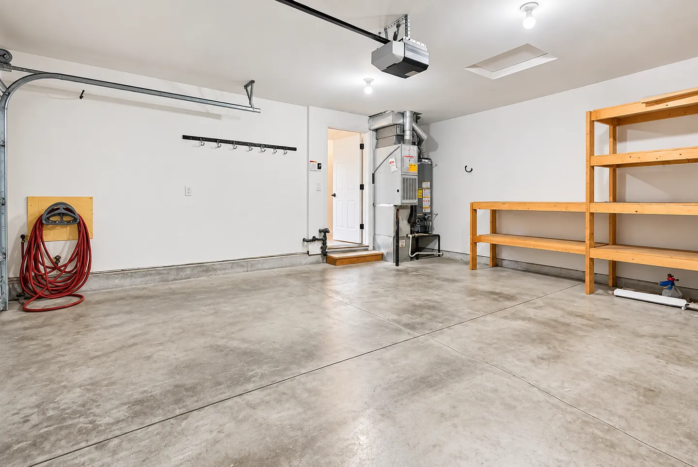 Well-lit empty garage with concrete floors, white walls, built-in wooden shelving, a water heater, and a doorway leading inside.
