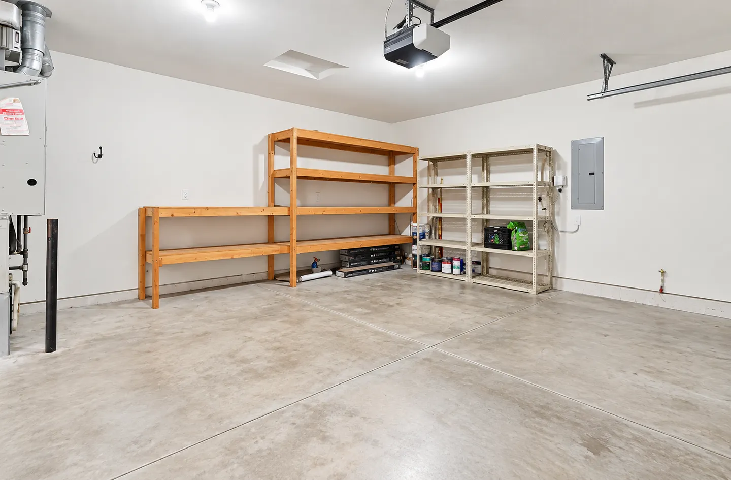 An empty garage interior featuring concrete flooring, white walls, and built-in wooden and metal storage shelving units.