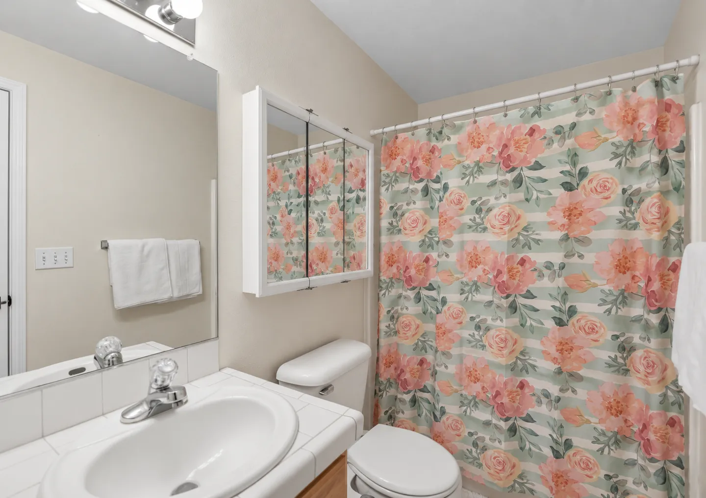 Bathroom showing a tiled vanity with sink, mirror, toilet, medicine cabinet, and floral shower curtain.