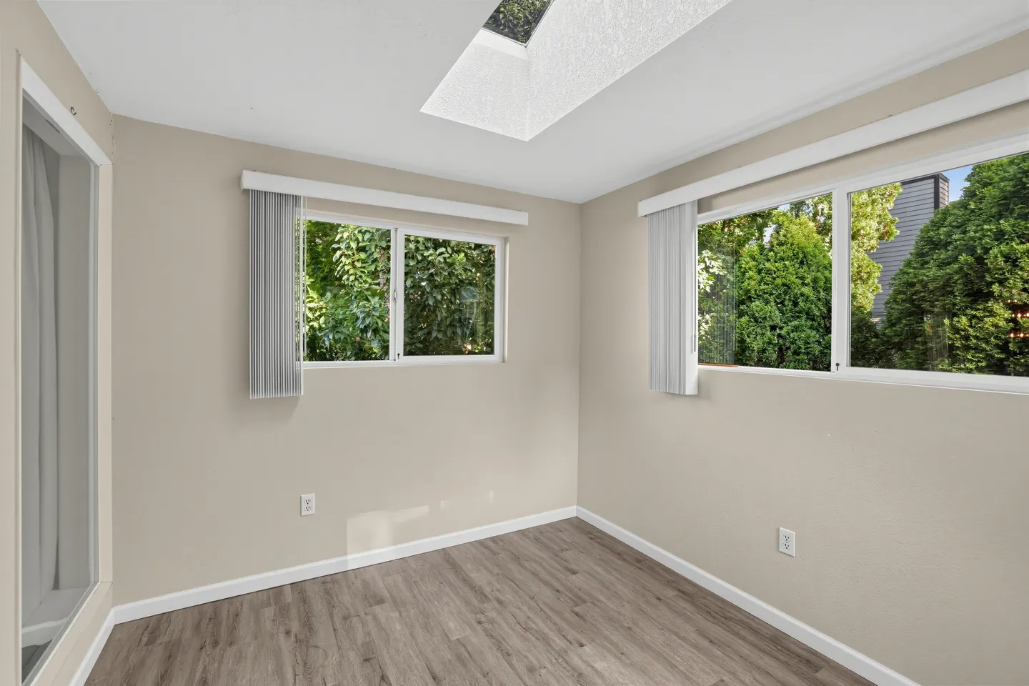 Empty room with wood-style flooring, light-colored walls, two sliding windows, and an overhead skylight.