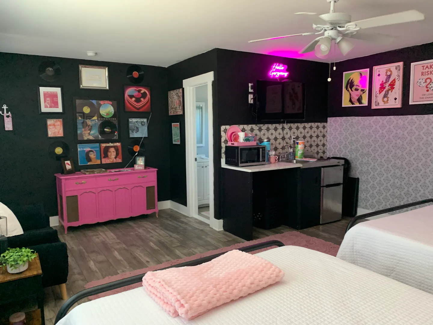 Bedroom with black walls, pink furniture accents, vinyl records decor, a kitchenette counter, and two beds.
