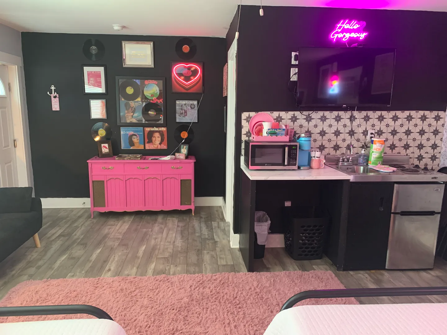 Interior room featuring black accent walls, a hot pink painted console table with vinyl records displayed above it, and a kitchenette counter with a mini fridge and microwave.