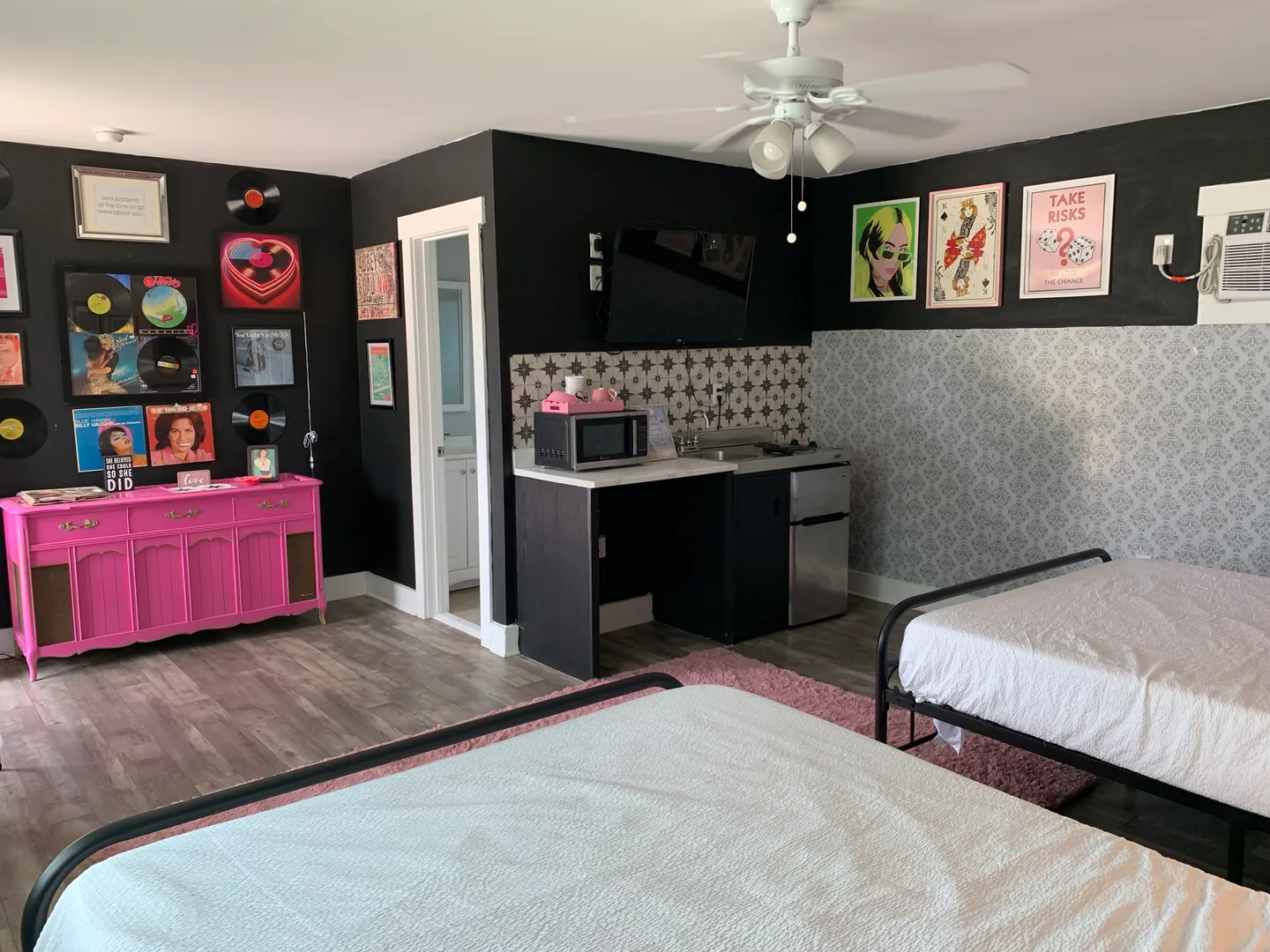Bedroom featuring two beds, a pink console cabinet, wall art with vinyl records, and a kitchenette counter with a mini fridge and microwave.