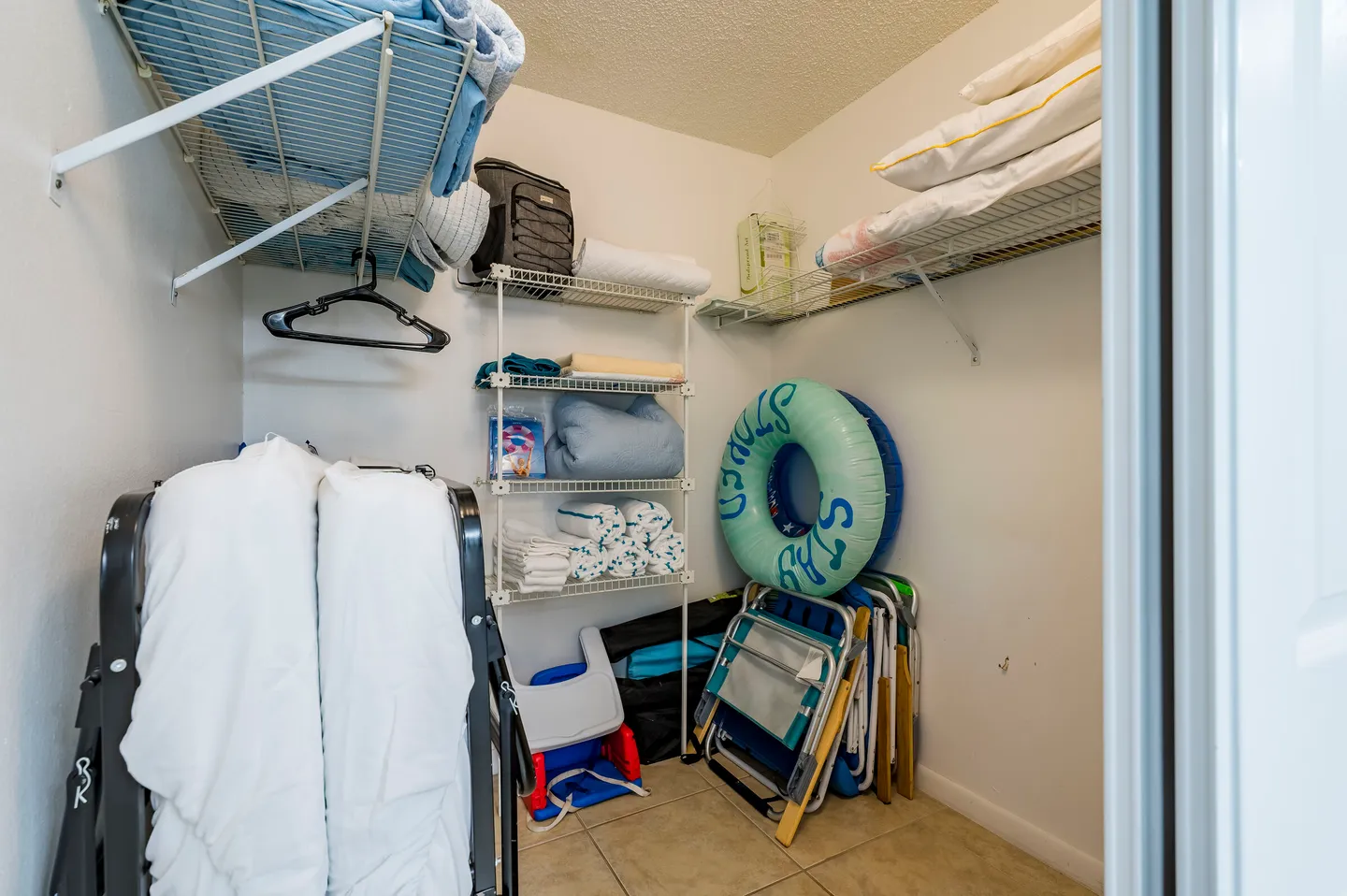 A storage closet stocked with folded linens, extra pillows, rollaway beds, beach chairs, and an inflatable pool ring.