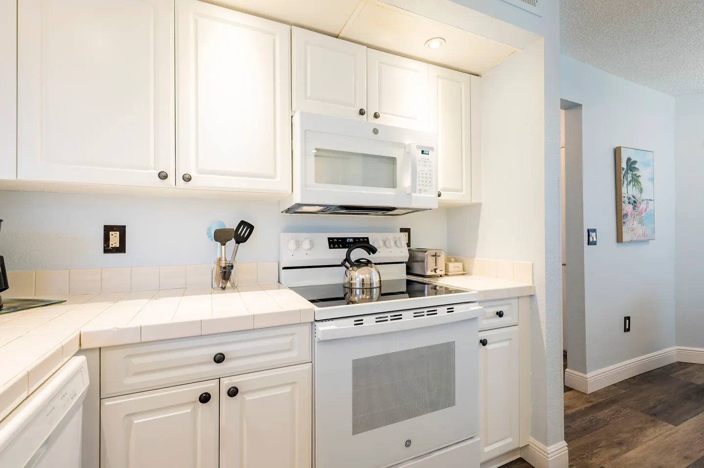 Kitchen counter with white cabinetry, tile countertop, white electric stove, and an over-the-range microwave.