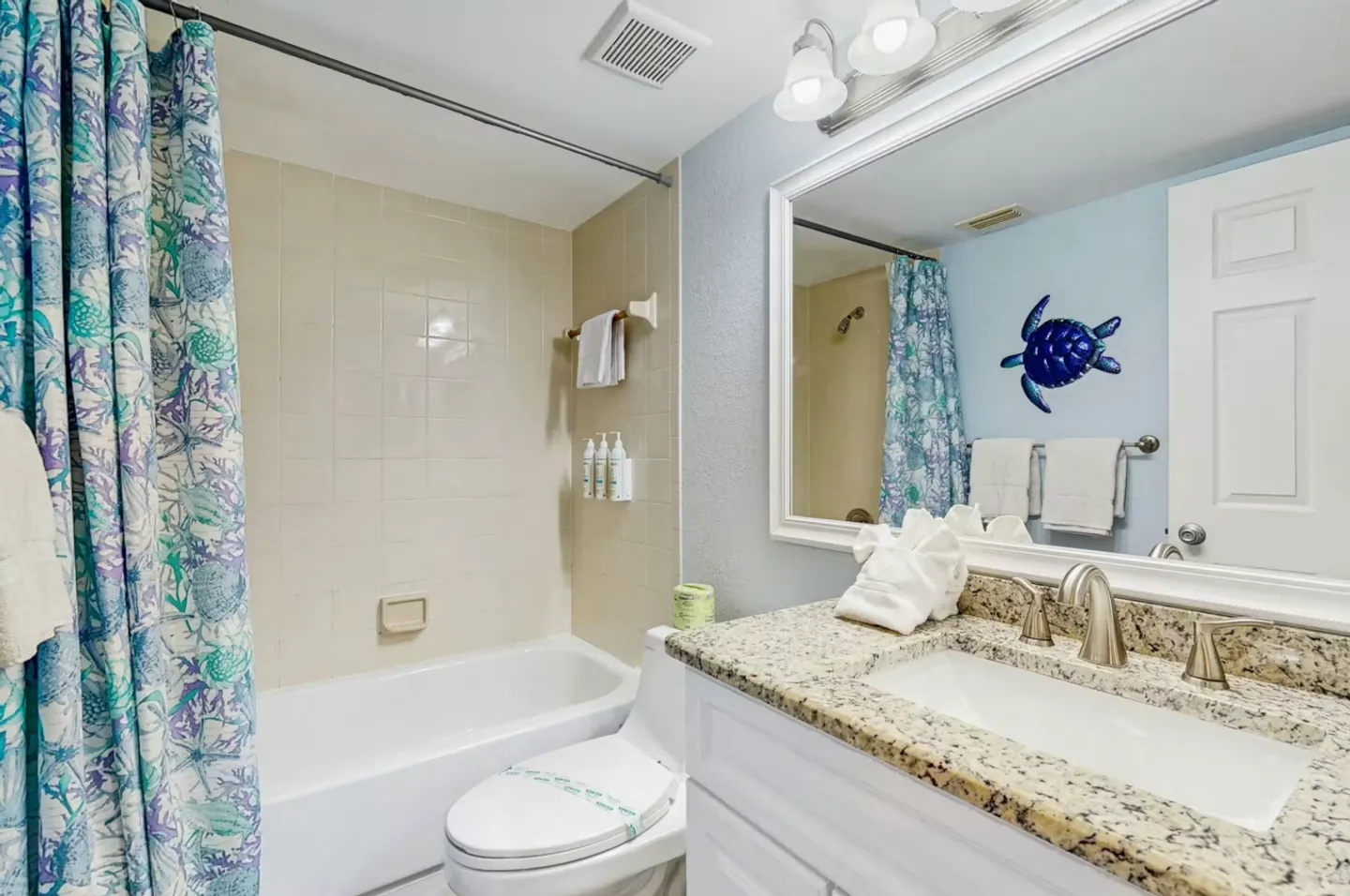 Bathroom with a granite-topped white vanity, framed mirror, toilet, and combination bathtub and shower with a sea turtle print shower curtain.