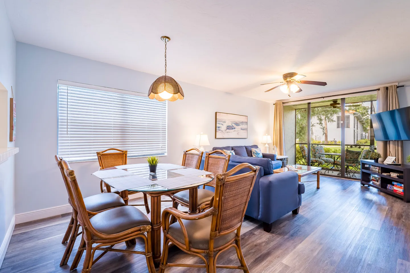 Open concept dining and living area featuring a dining set with wicker chairs, a blue sofa, and sliding glass doors leading to an outdoor patio.