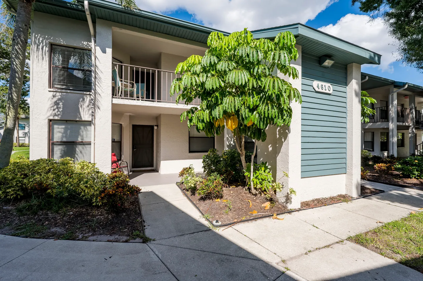 Exterior view of a two-story residential building with a concrete walkway, landscaping, and a ground-floor covered entrance.
