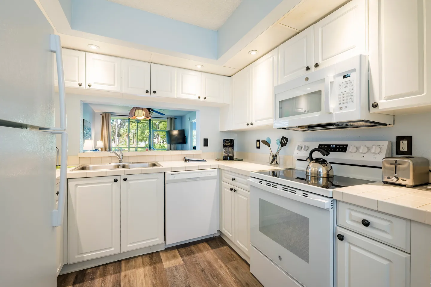 Kitchen with white cabinetry, white appliances, tiled countertops, and a pass-through opening to the living area.