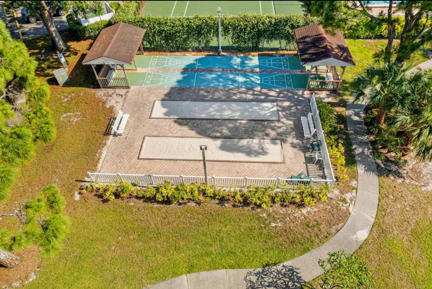 Aerial view of outdoor community recreation courts including shuffleboard and bocce ball surrounded by grass, trees, and small gazebos.