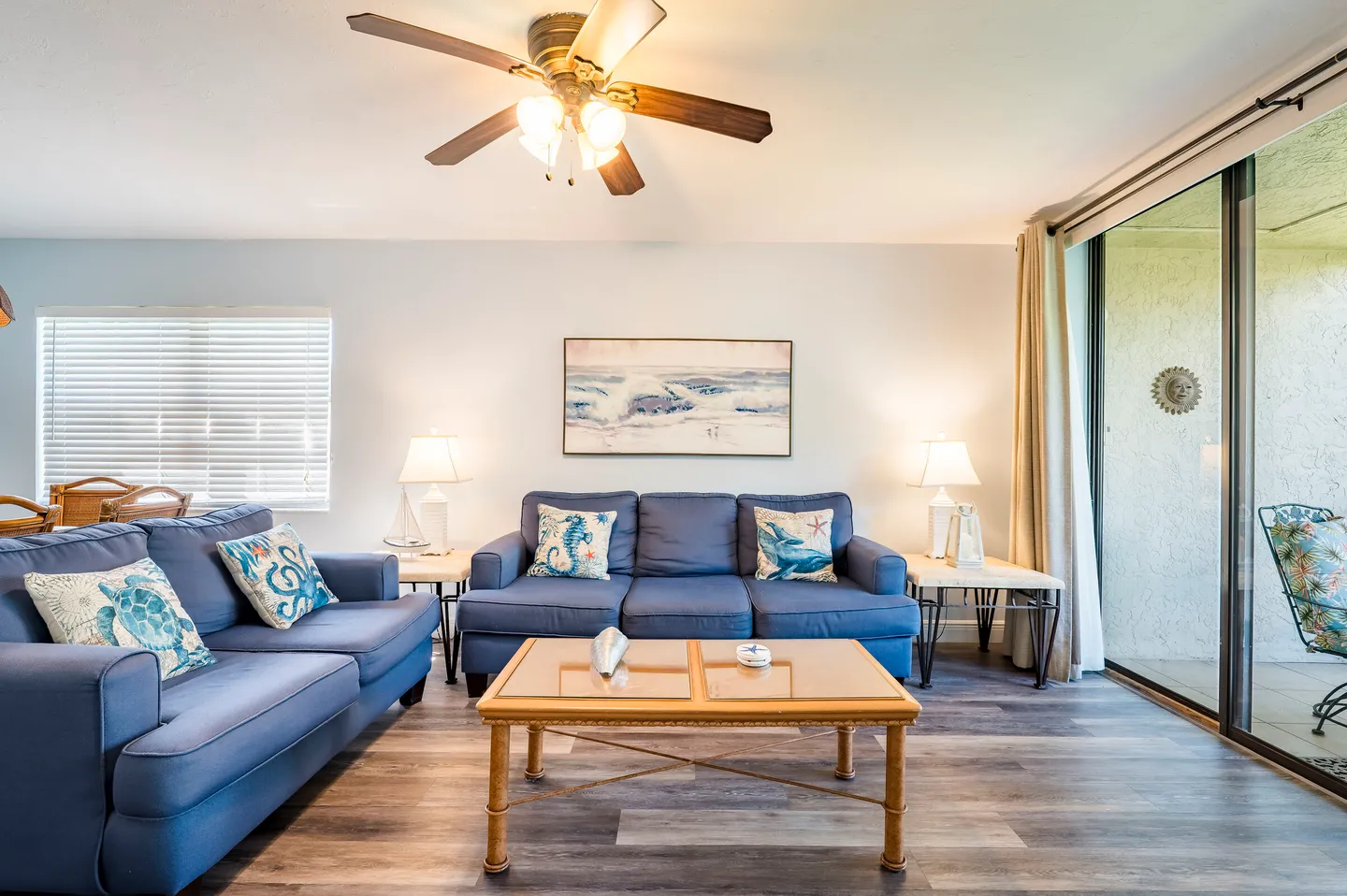 Living room with blue upholstered sofas, a wooden coffee table, a ceiling fan, and sliding glass doors leading outside.