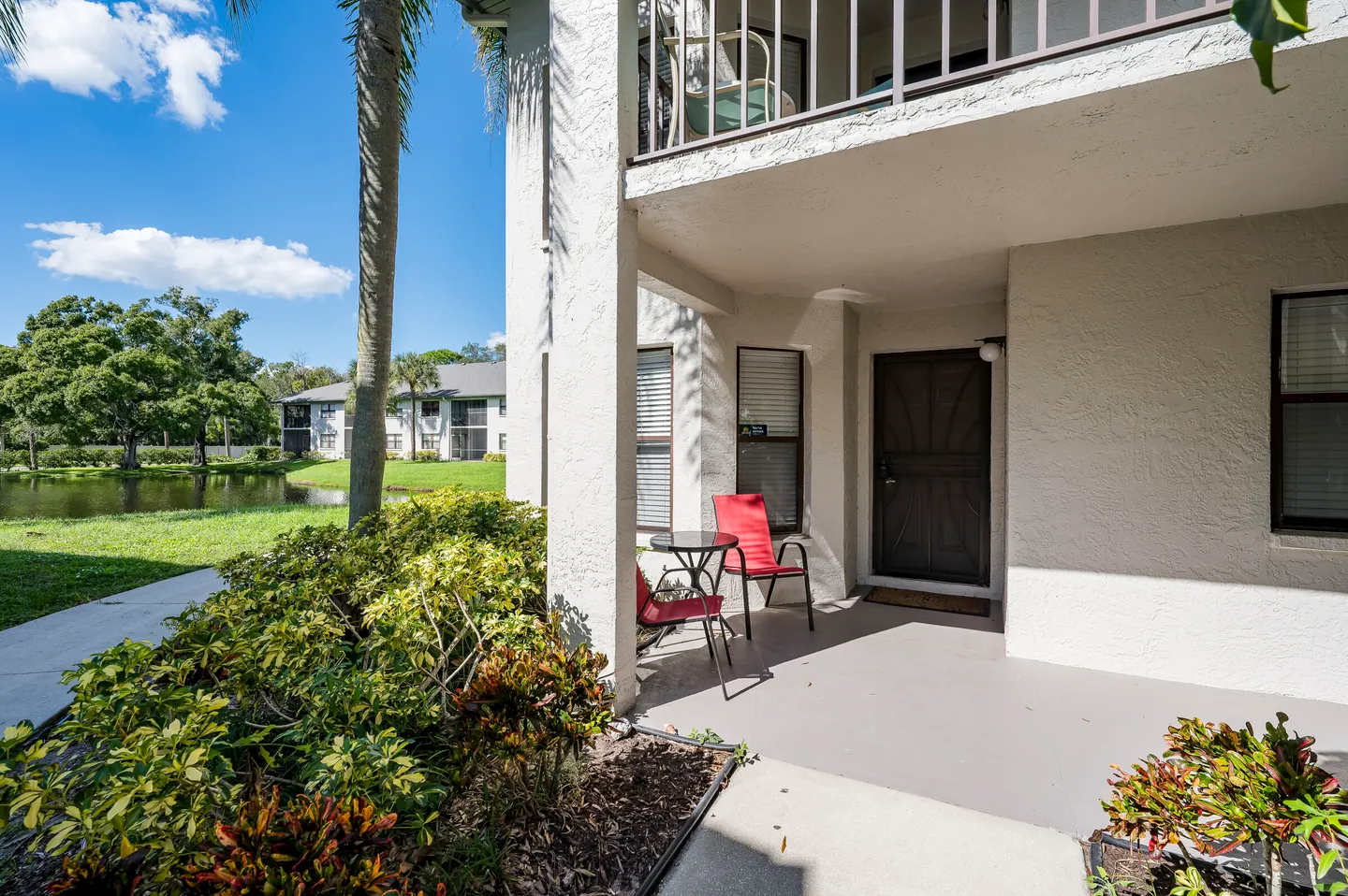 Covered ground-floor entryway patio with outdoor chairs and table next to landscaping and a water view.