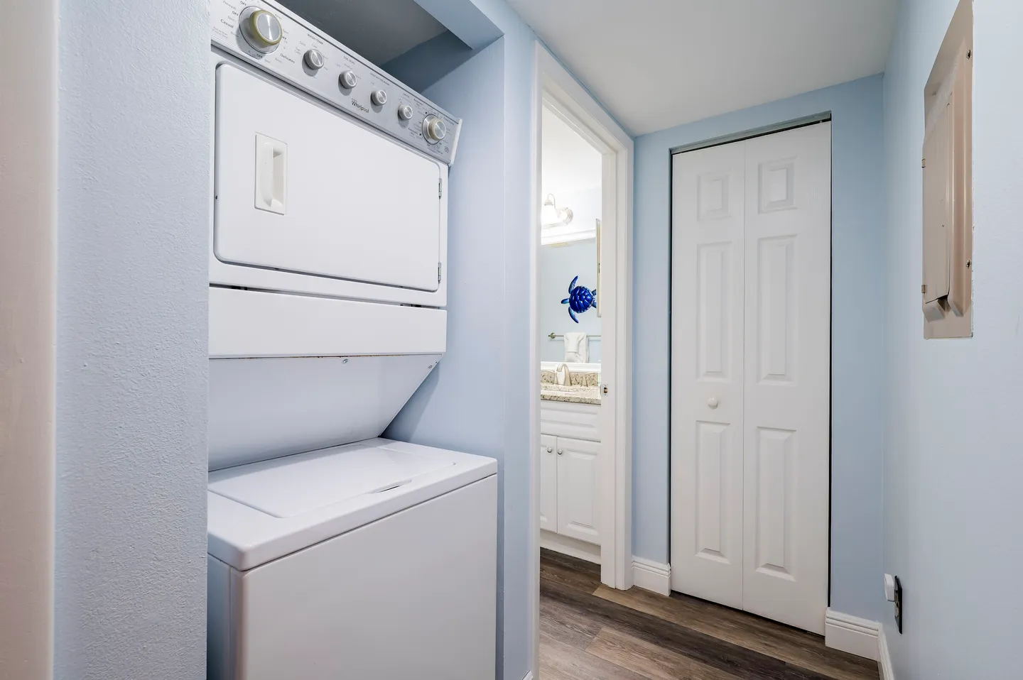 A stacked white washer and dryer unit in a hallway alcove next to a bathroom doorway.