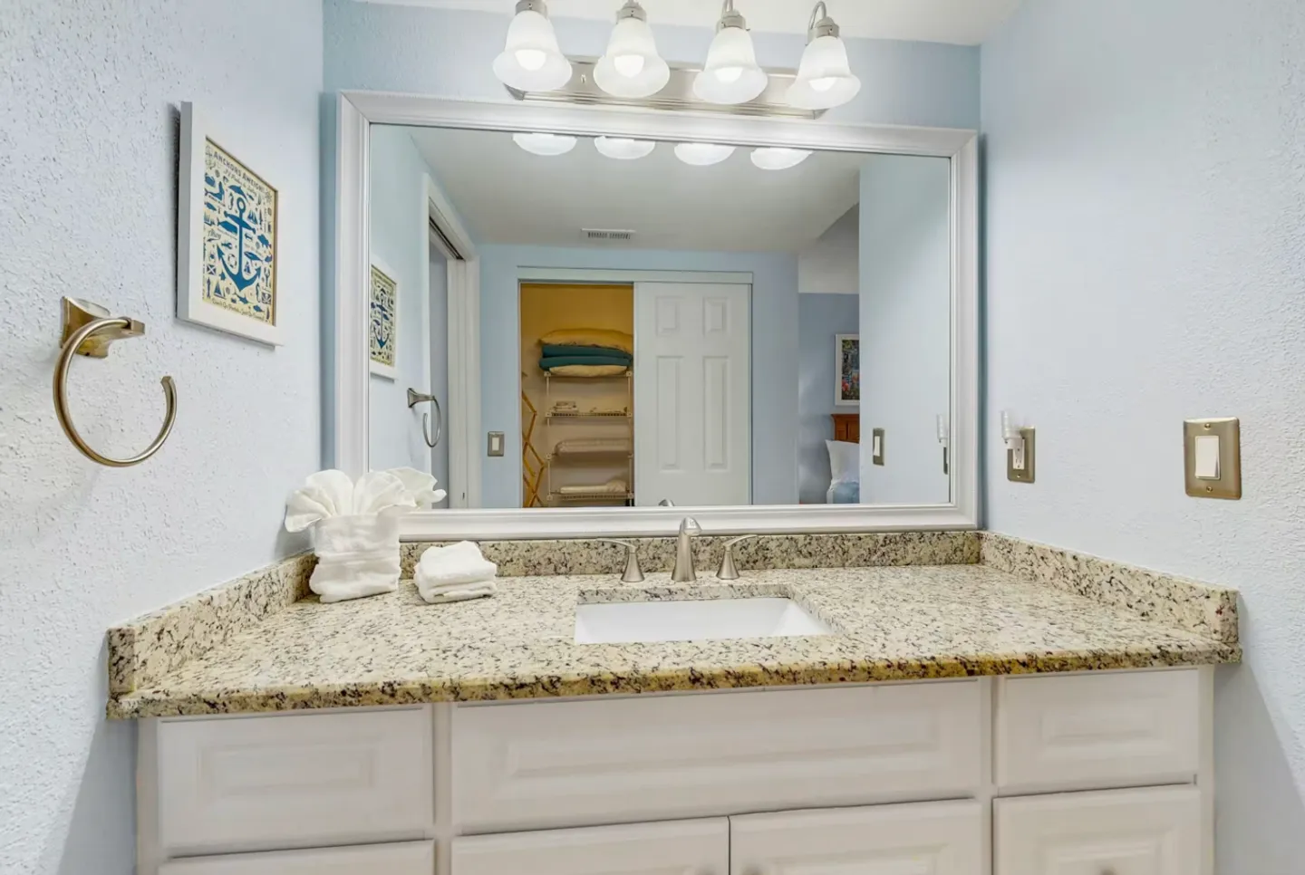 Bathroom vanity with a speckled countertop, undermount sink, large framed mirror, and overhead light fixture.
