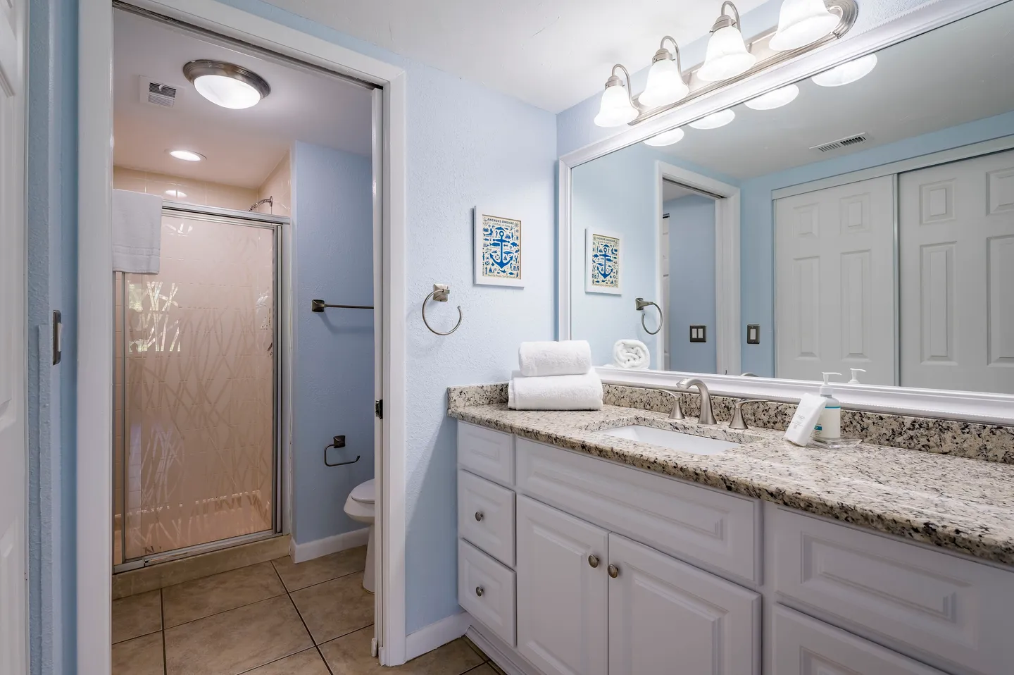 Bathroom with white vanity, speckled countertop, large mirror, and view into an adjacent shower and toilet area.