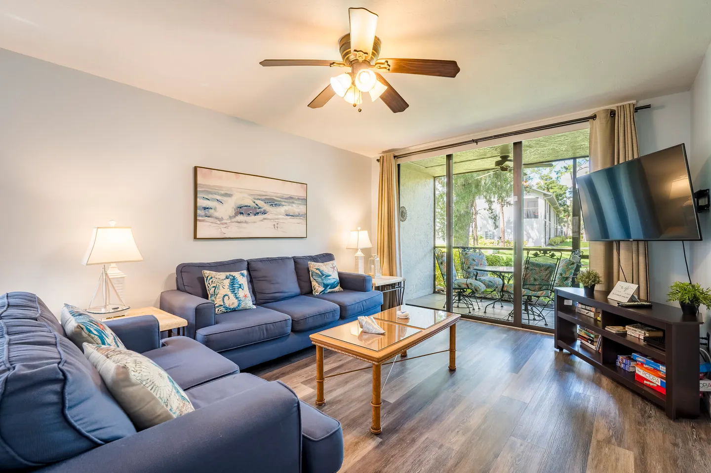 Living room with blue sofas, a coffee table, a TV on a media console, and sliding glass doors leading to a screened porch.