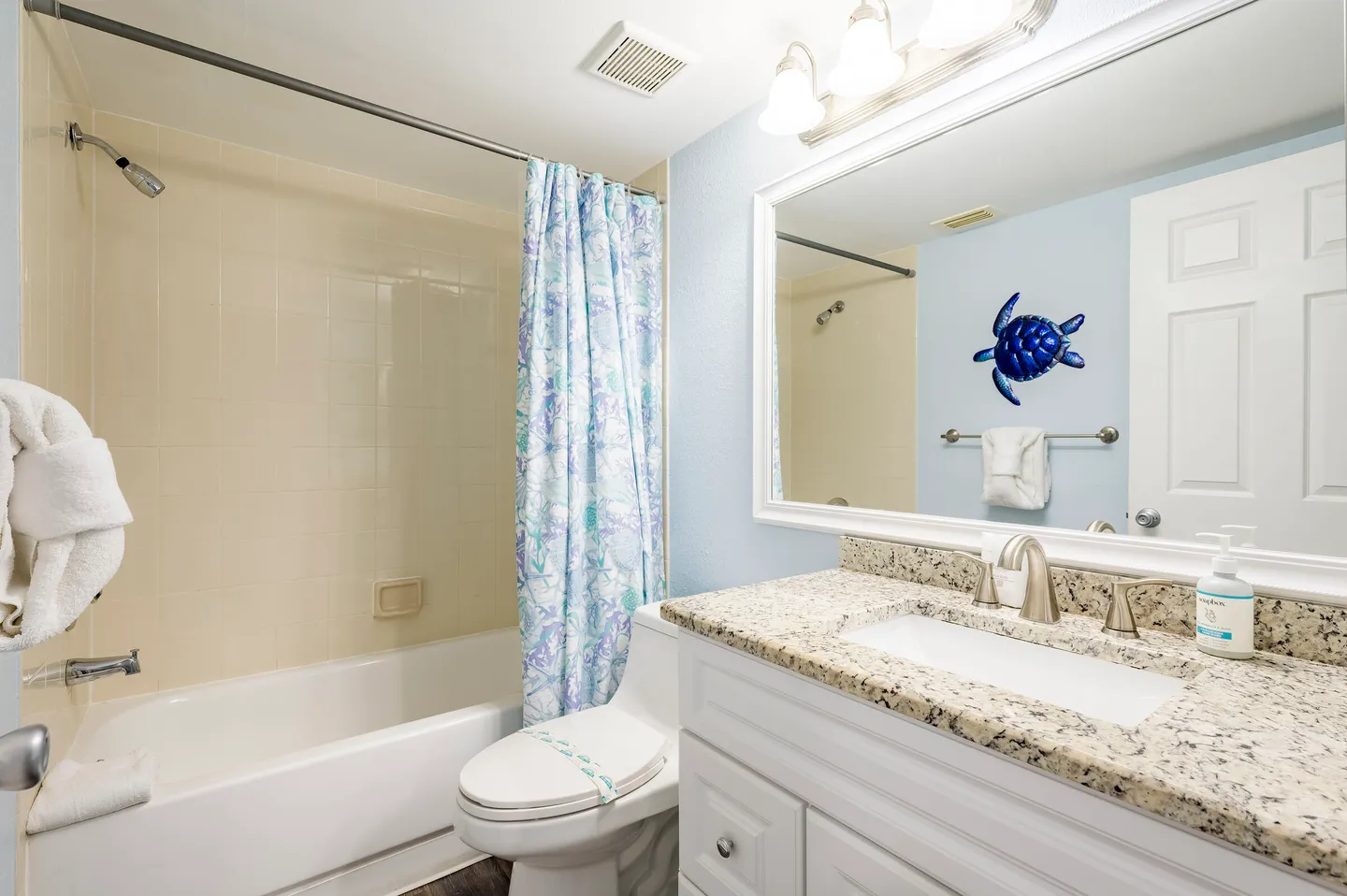 Bathroom with a white bathtub and shower combination, toilet, and vanity with speckled countertop and large mirror.