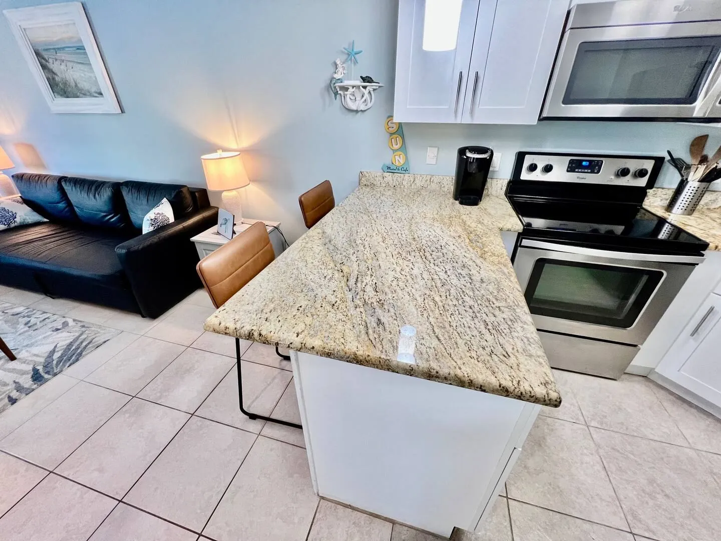 Kitchen counter peninsula with barstools next to a stove and adjacent to a living area with a black sofa.