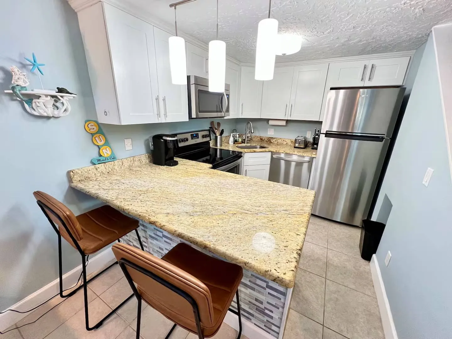 Kitchen featuring a breakfast bar with two brown barstools, speckled countertops, white cabinets, and stainless steel appliances.