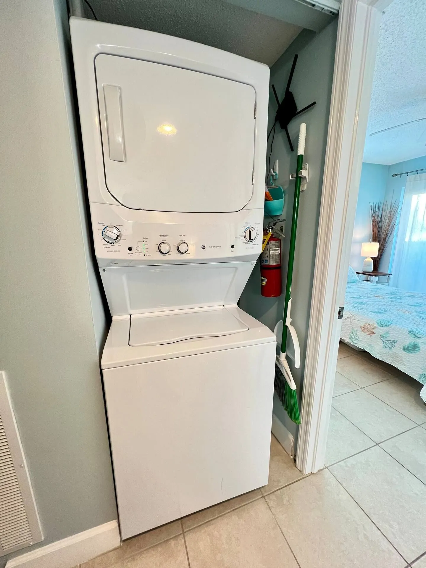 A stacked white washer and dryer unit tucked inside a closet alcove adjacent to a bedroom doorway.