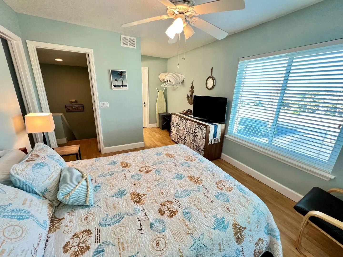 Bedroom with sea-themed bedding, light blue walls, a TV on a dresser, and a window with blinds.