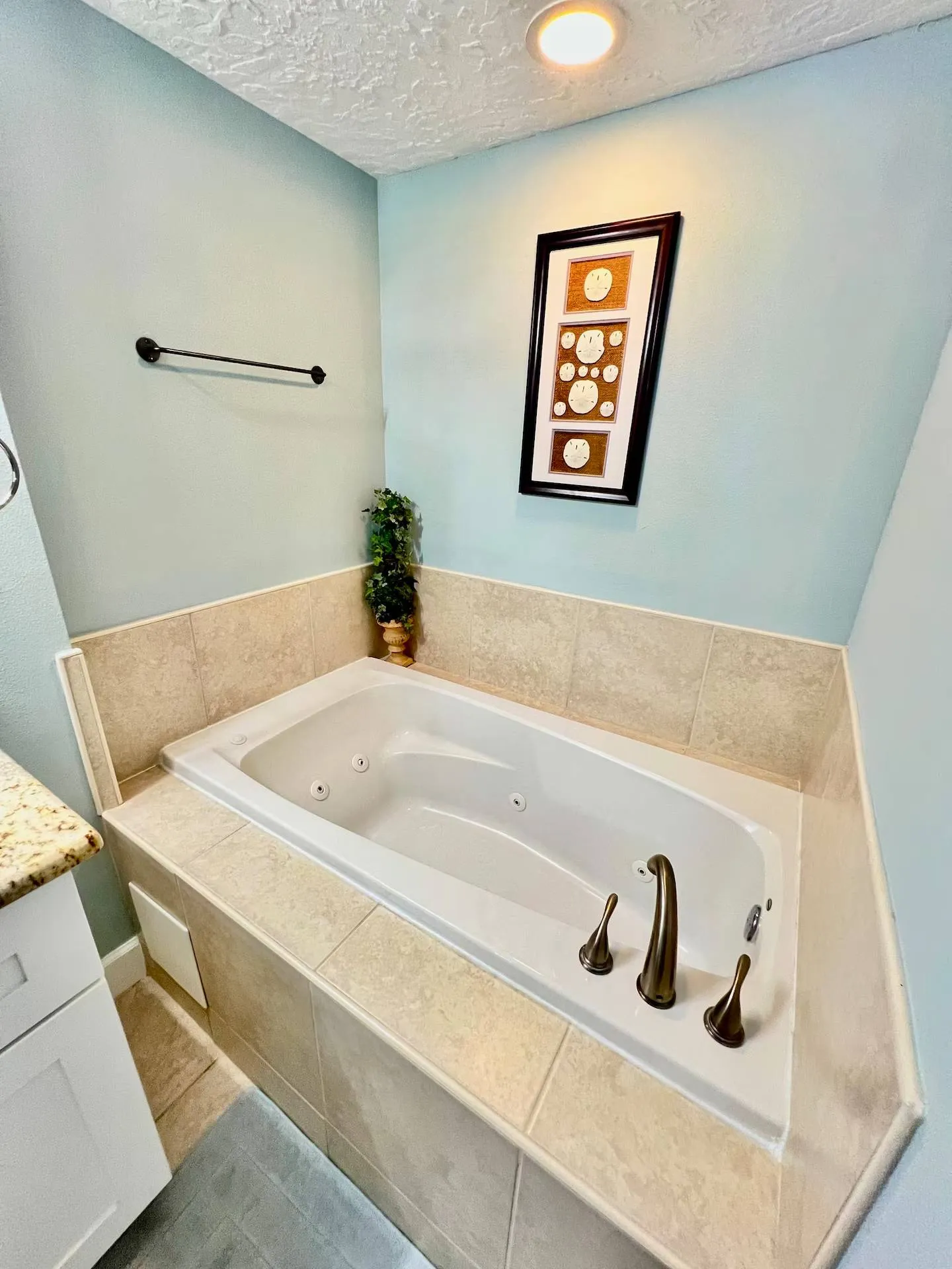 A built-in jetted soaking tub with beige tile surround set into a light blue bathroom alcove.
