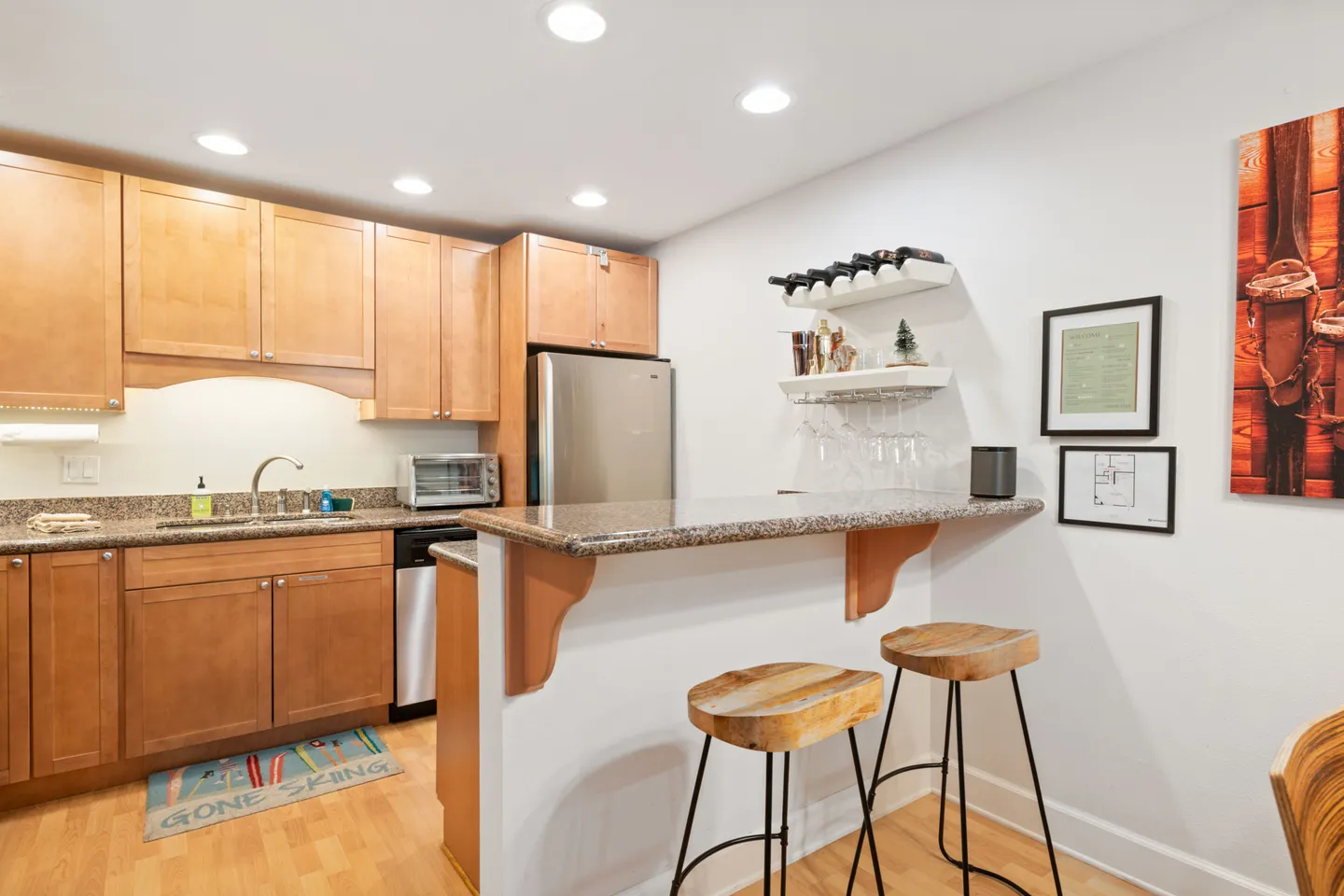 Kitchen with wooden cabinetry, speckled countertops, breakfast bar with two backless bar stools, and stainless steel refrigerator.