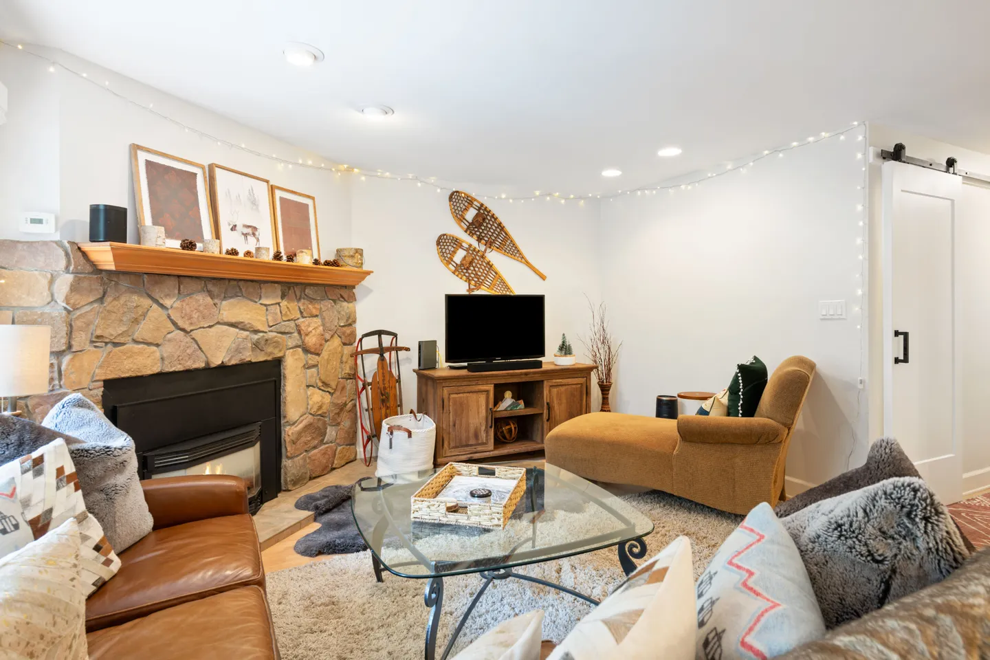 Cozy living room with a stone-clad fireplace, glass coffee table, leather sofa, chaise lounge, and a television.