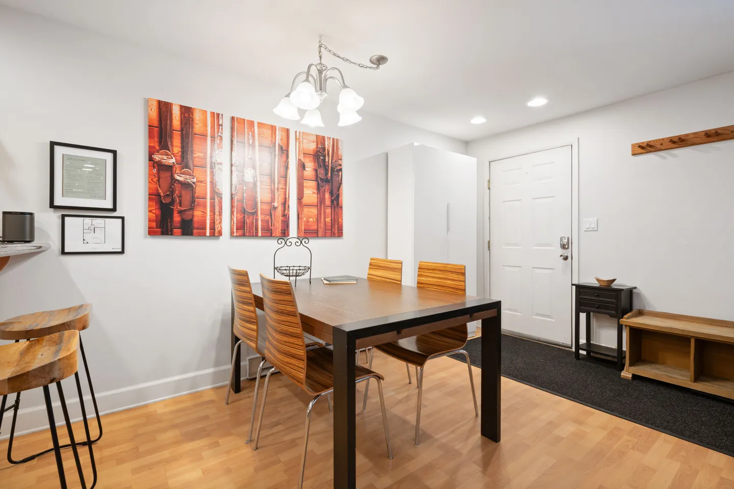 Dining area with a wooden table, bentwood chairs, an overhead chandelier, and a front entry door with a coat rack and entryway bench.